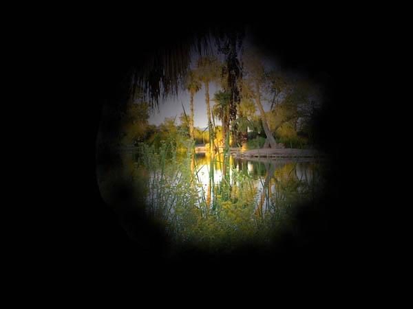 Landscape of trees and lake obscured by black border on all sides. 